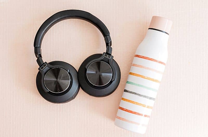 Des écouteurs et une bouteille d'eau réutilisable sont des exemples d'articles à inclure dans son bagage de cabine. Un visuel du blog Pour un bonheur simple.